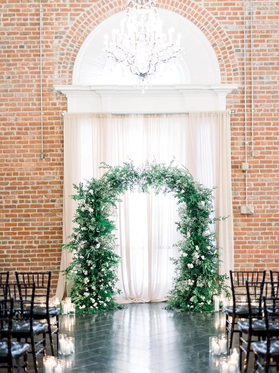 Greenery ceremony arch beneath a ballroom chandelier