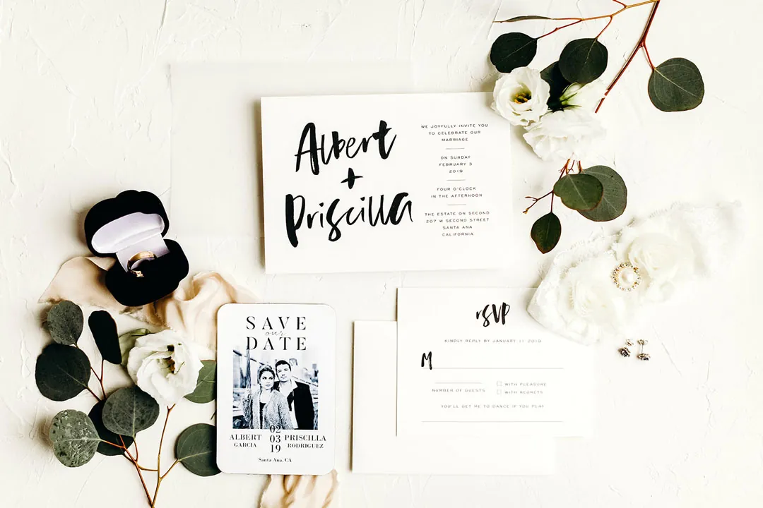 Wedding invitations arranged with rings, flowers, and greenery