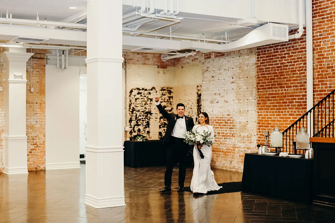 Couple standing in an open reception room with brick walls