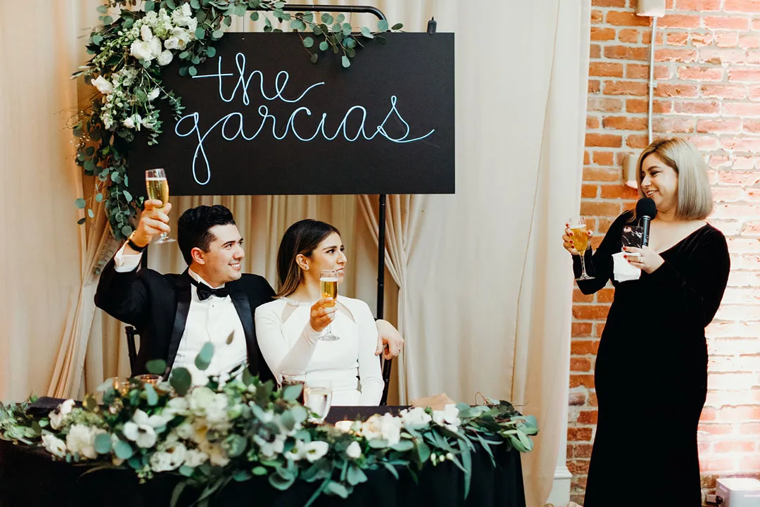 Guest giving a toast beside the couple's flower-lined table