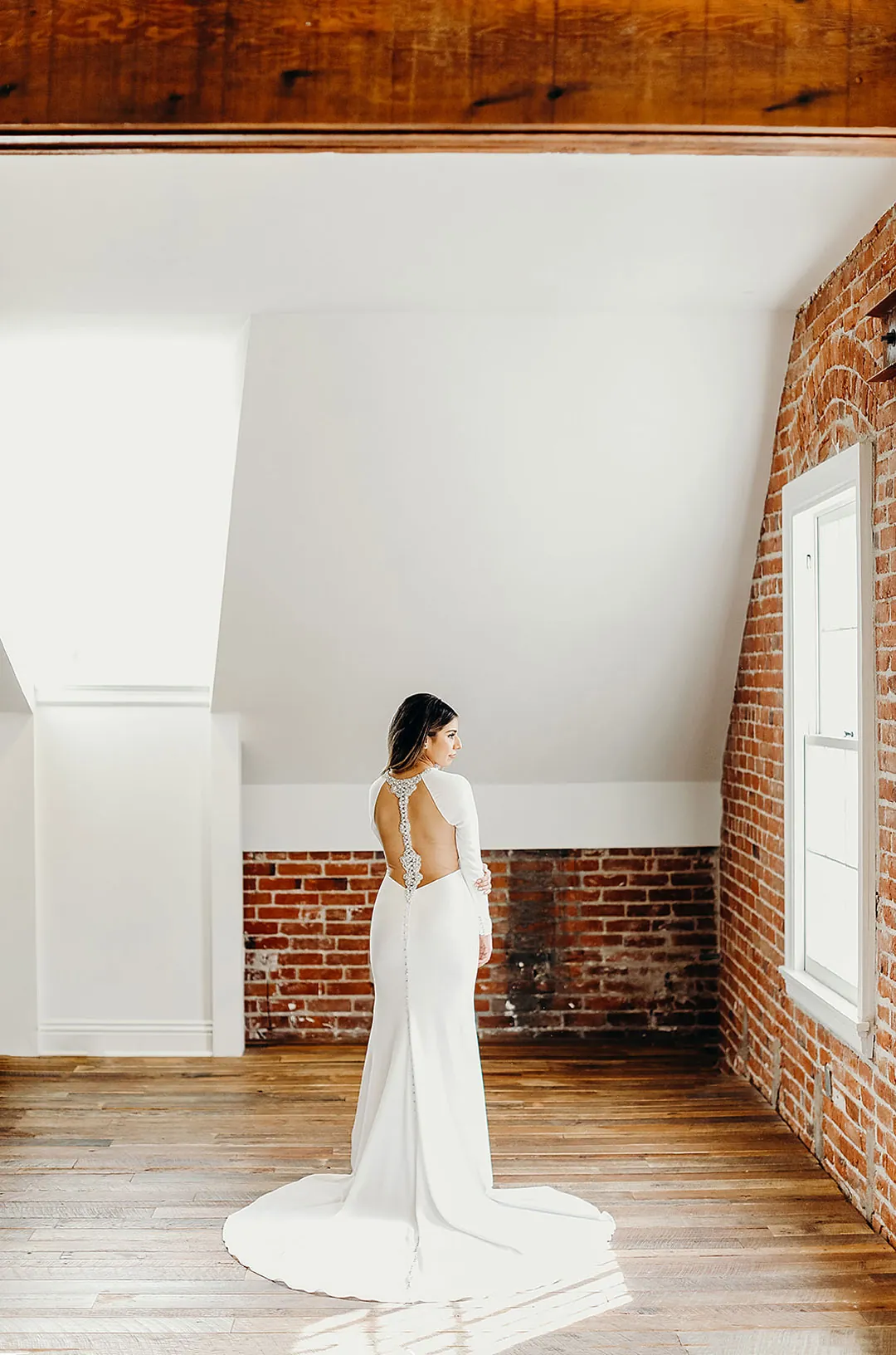 Bride standing beneath exposed wooden beams in a brick-walled room