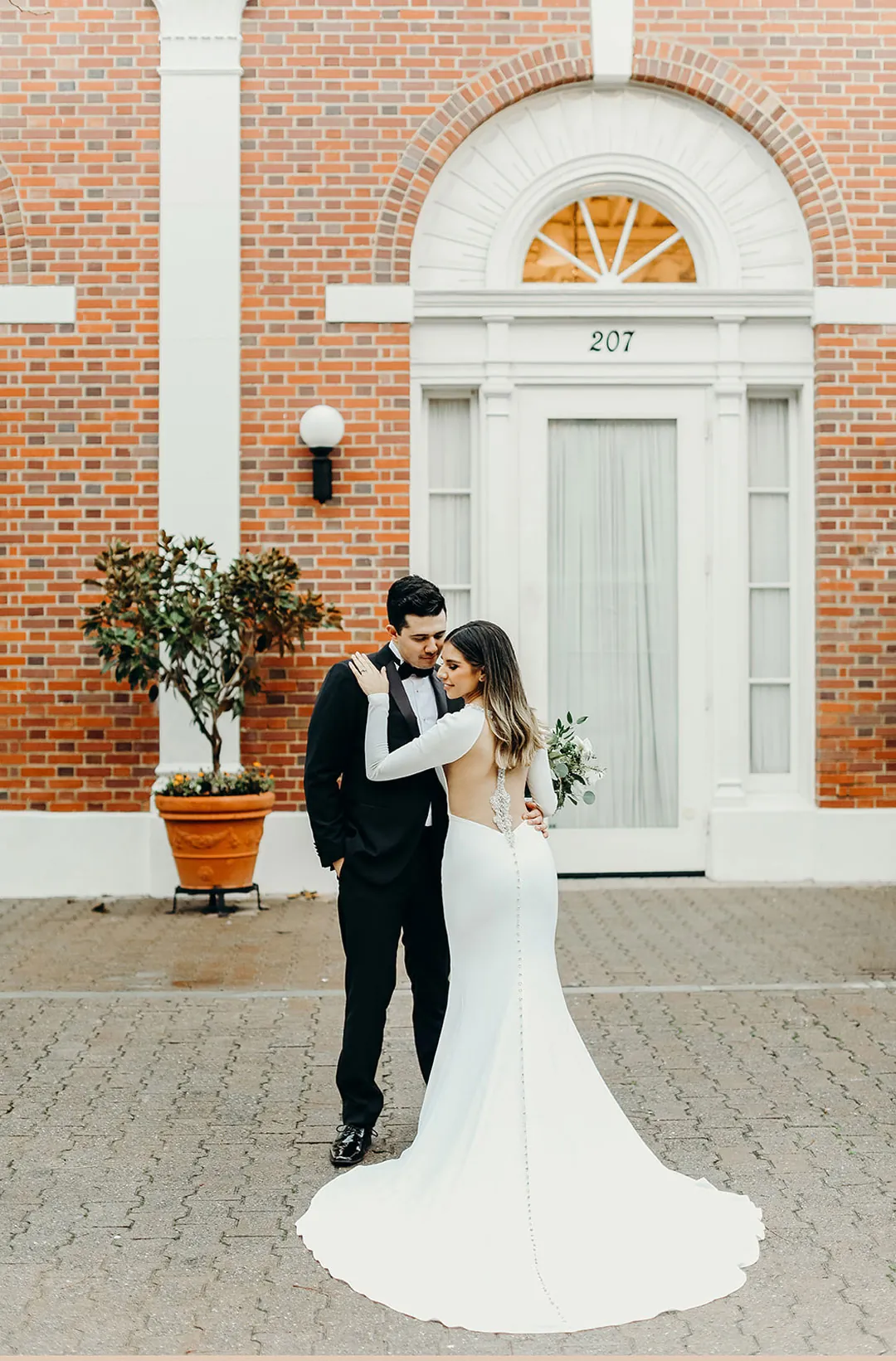 Couple embracing outside a white doorway in a brick building