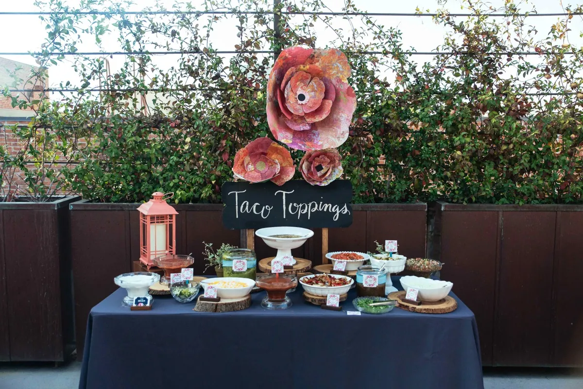 Taco toppings table decorated with large colorful paper flowers