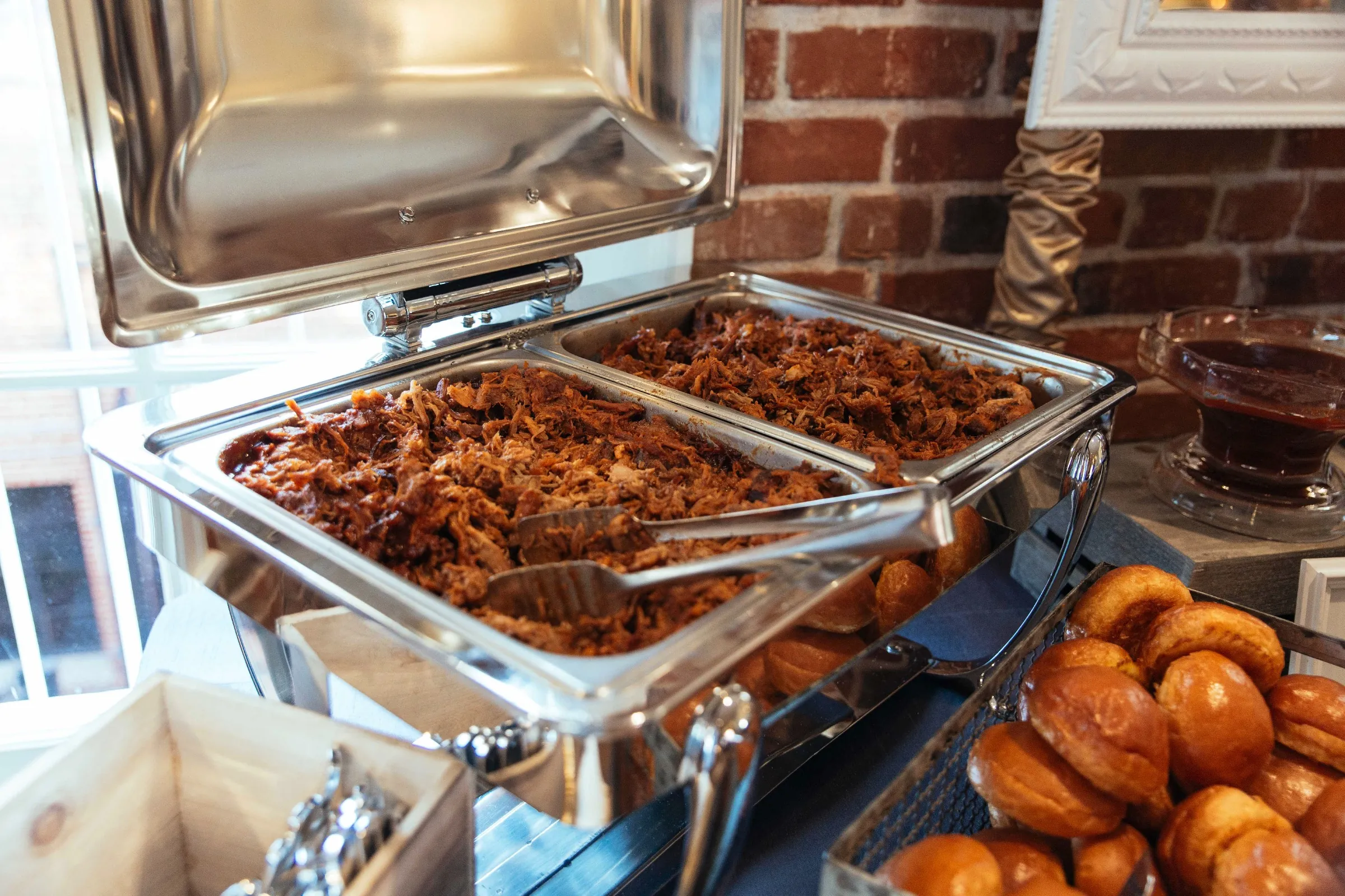 Buffet tray of cooked meat beside bread rolls