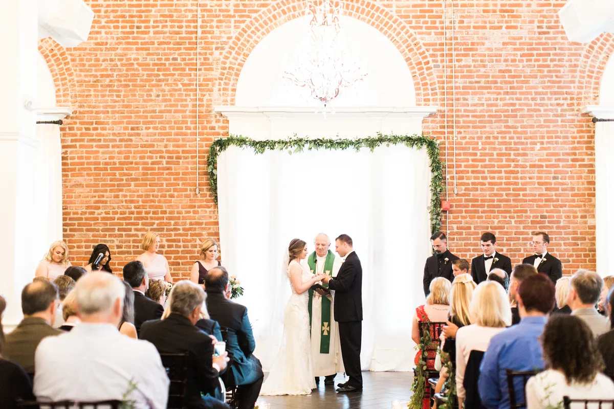Guests watching a ballroom ceremony before a white floral backdrop