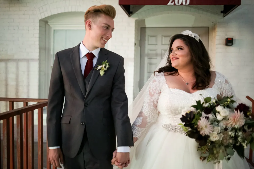 Bride and groom walk together outside, with the bride holding a white bouquet.