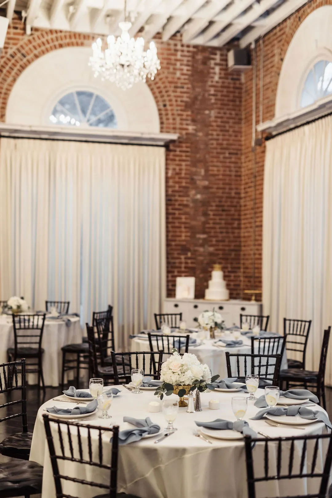 Round reception table with white flowers, blue-gray napkins and black chairs.