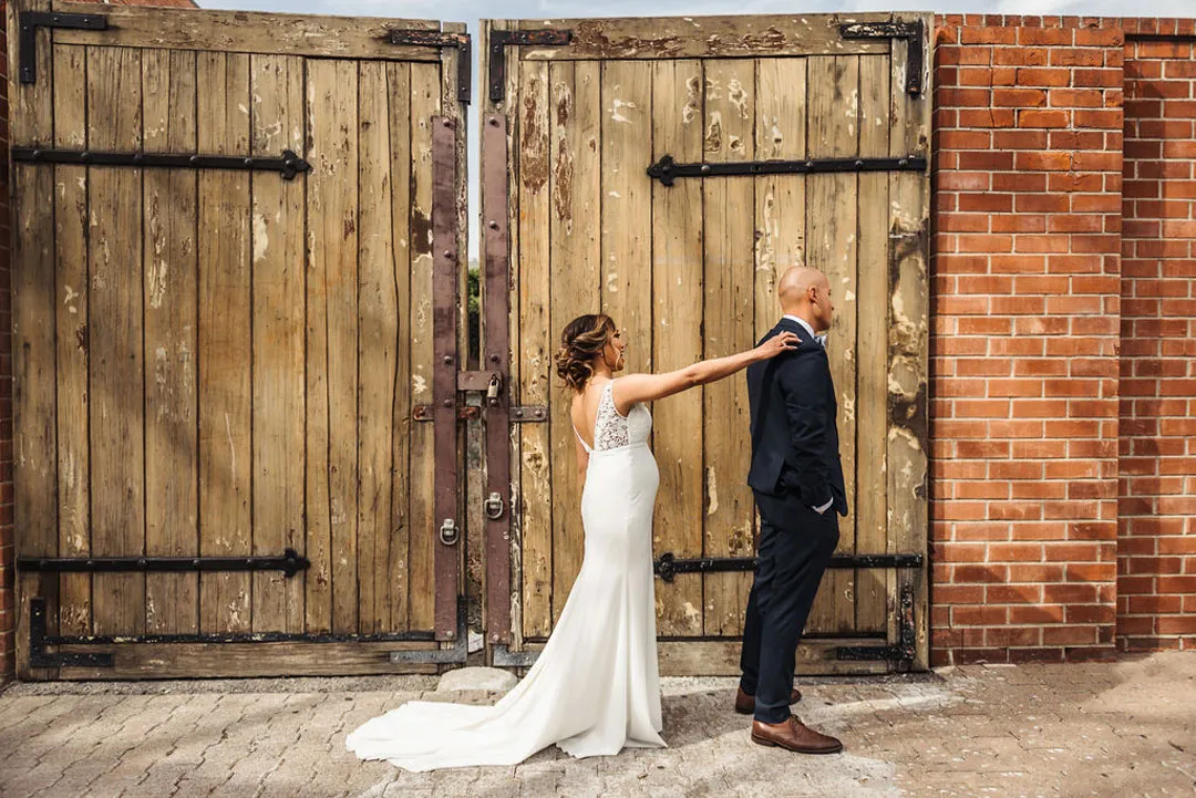 Bride reaches for the groom’s shoulder during a first look beside wooden doors.