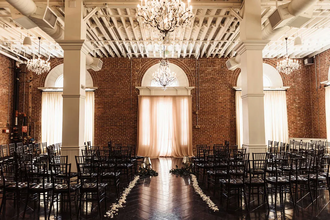Ballroom ceremony aisle lined with white petals between rows of black chairs.
