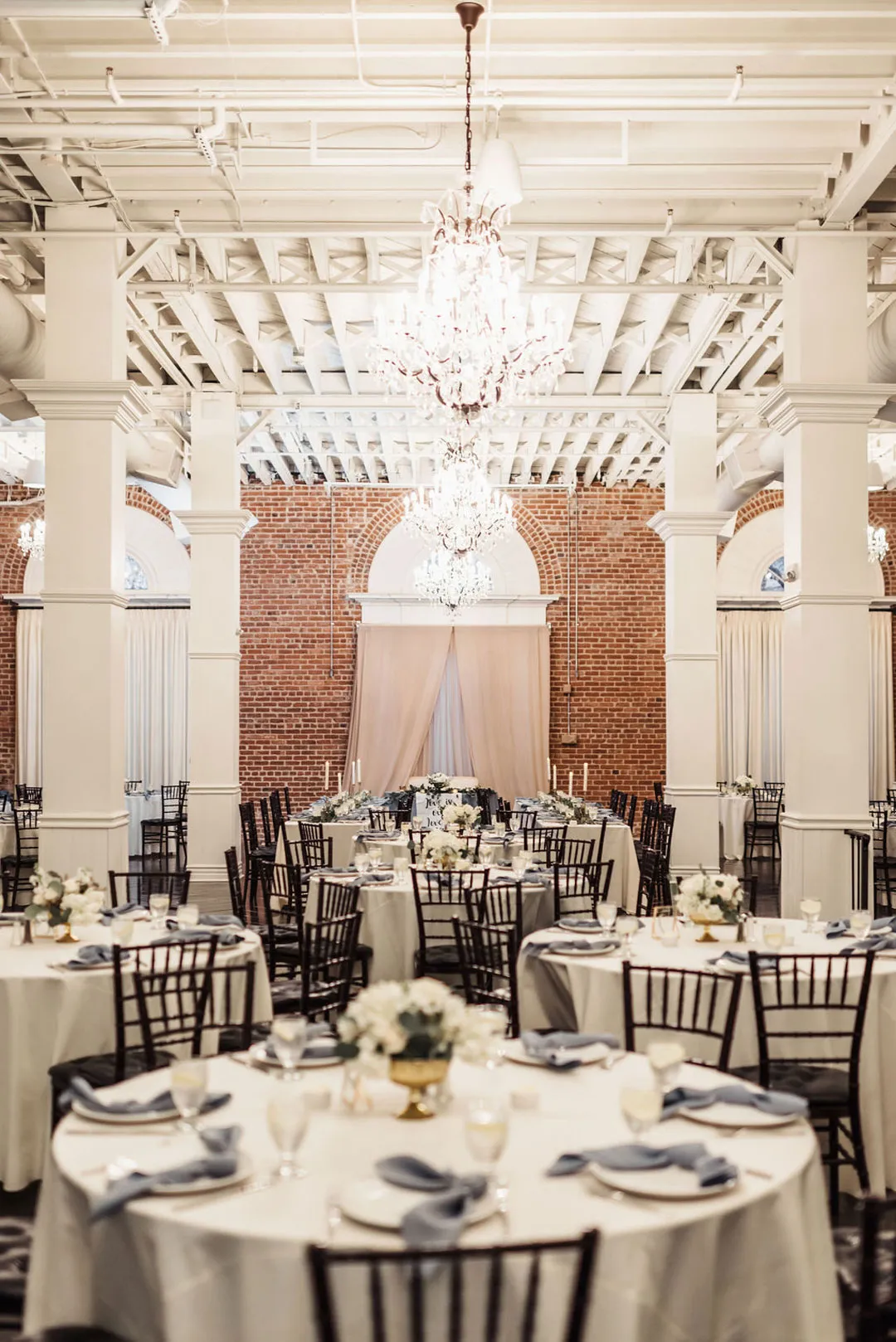 Ballroom reception tables with white flowers, blue-gray napkins and chandeliers.