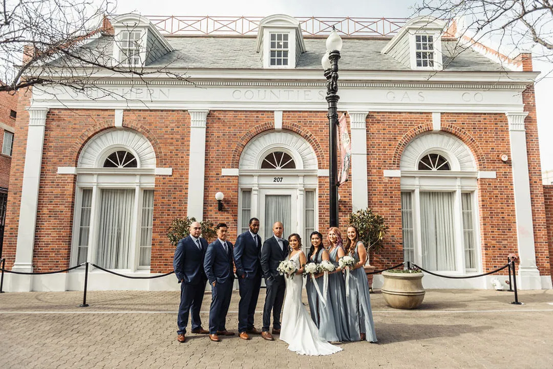 Wedding party stands outside the red-brick venue beneath its arched windows.