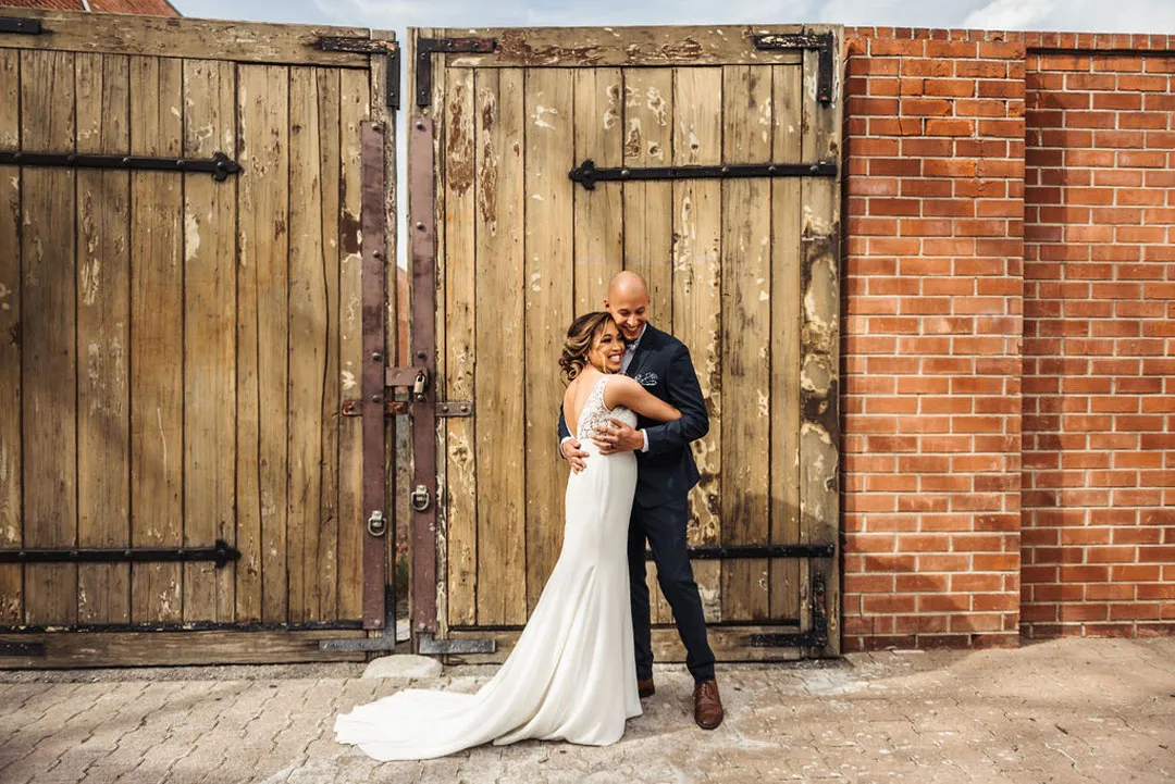 Bride and groom embrace beside wooden doors after their first look.