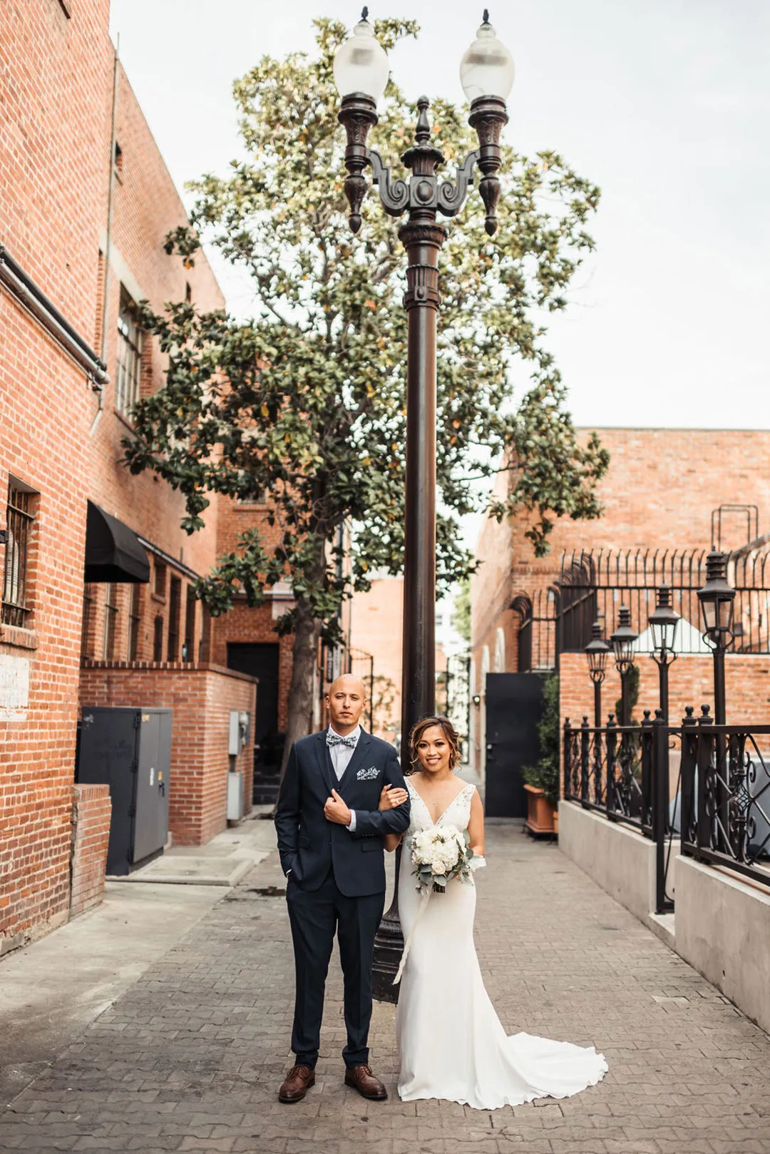 Bride and groom pose beneath a streetlamp on a brick-lined walkway.