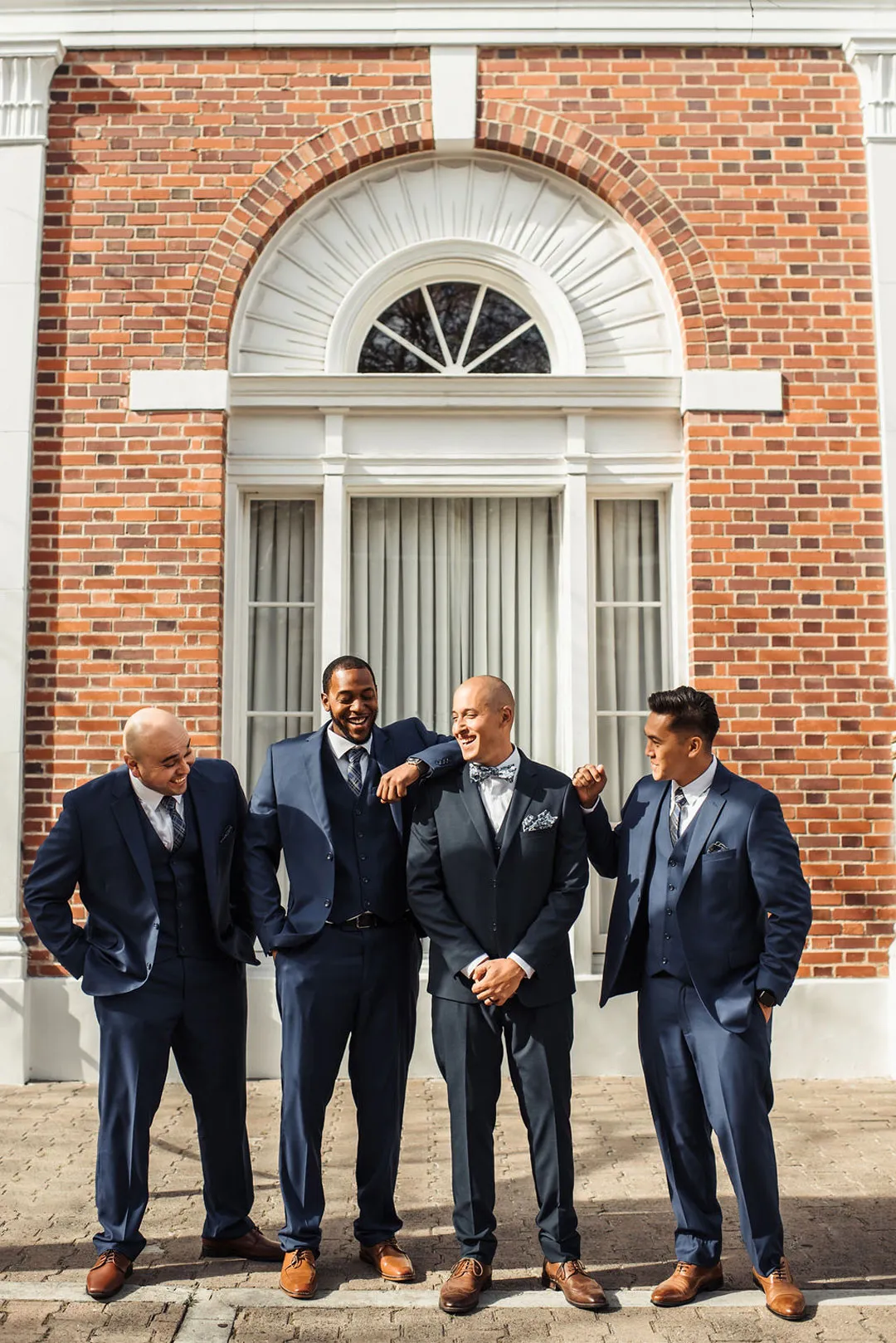 Groom and groomsmen laugh together outside the brick venue.