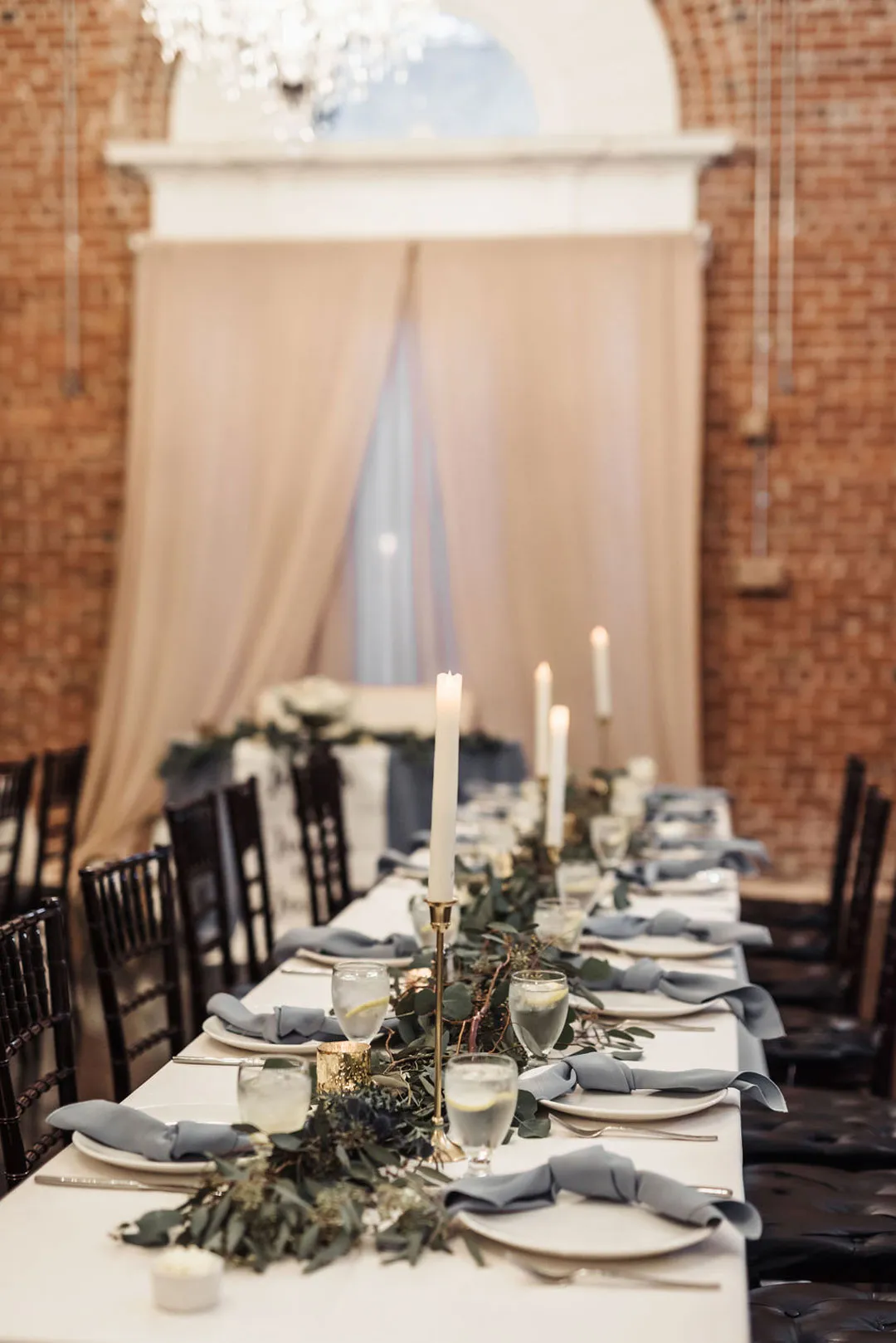Long reception table decorated with eucalyptus, tall candles and blue-gray napkins.