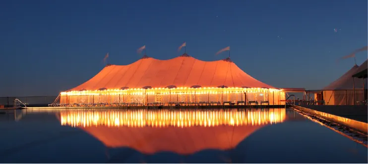 Sailcloth tent lit up at dusk, reflected in the water