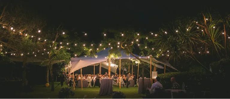 Wedding dinner at night under a white stretch tent with lights