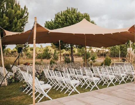 Sand-coloured stretch tent over a wedding ceremony with white chairs