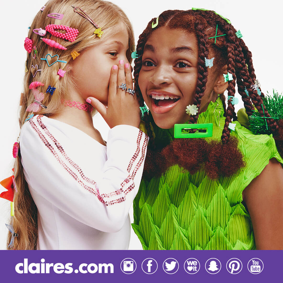 Two young girls with many Claire's hair accessories whispering to each other.