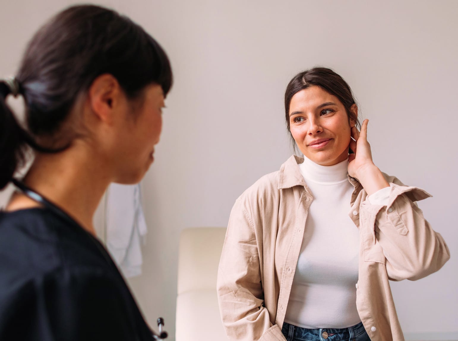 A female doctor talking to a woman who is touching her neck during a consultation.