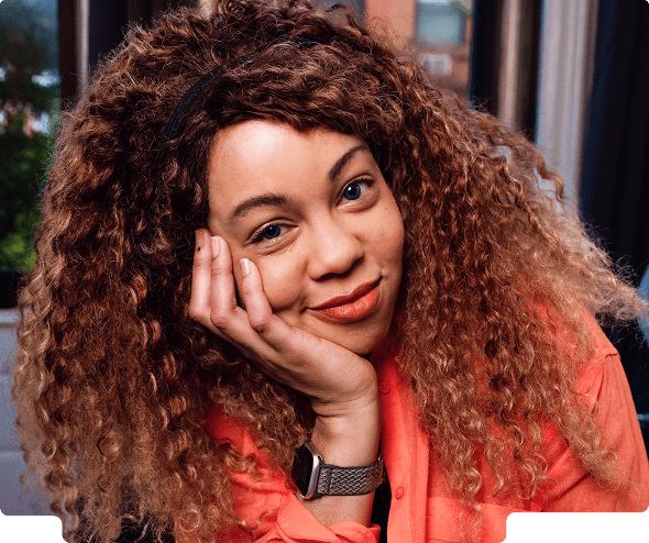 Woman with voluminous curly hair resting her face on her hand and smiling gently.
