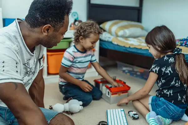 Two children playing with toys on the floor, while an adults watches them