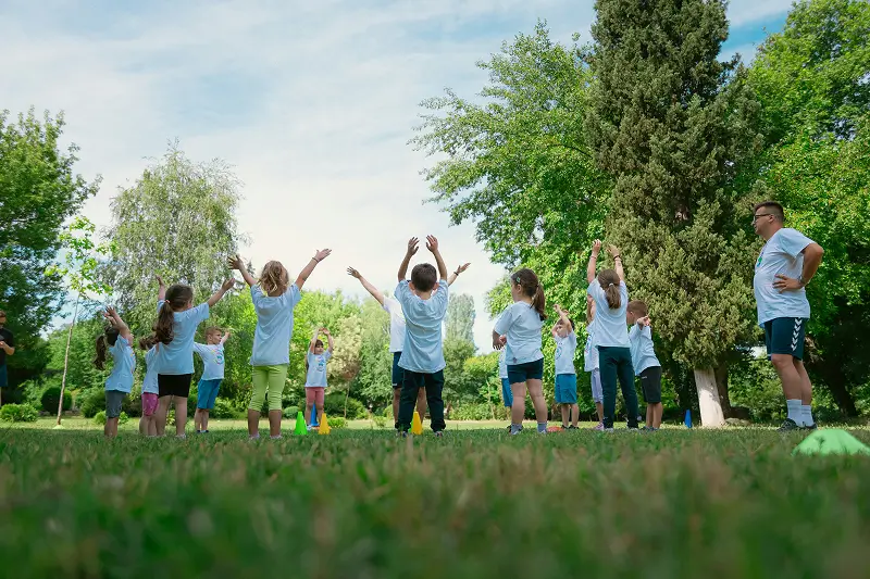 Group of children wearing matching t-shirts doing a group activity outside with an adult supervising
