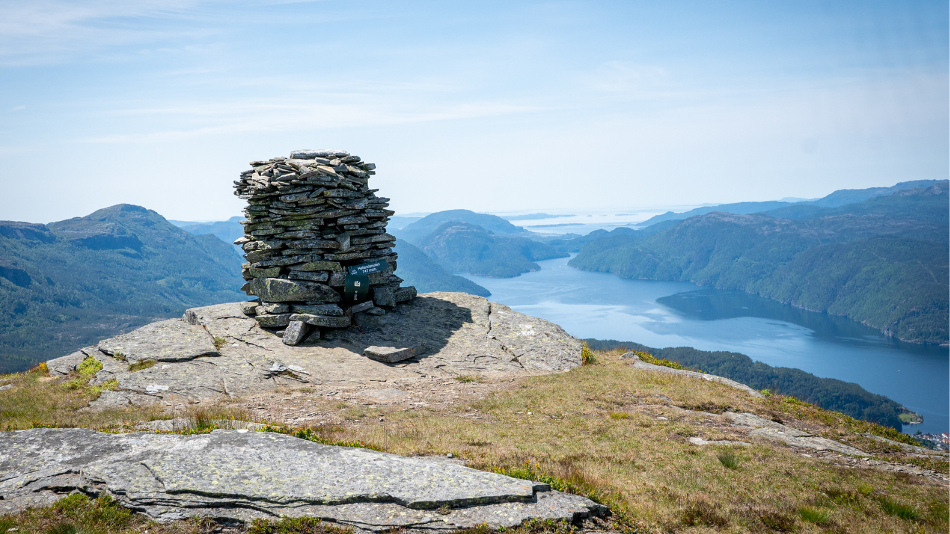 Ein person sit på ein åskam og ser ut over dalen i solnedgangen