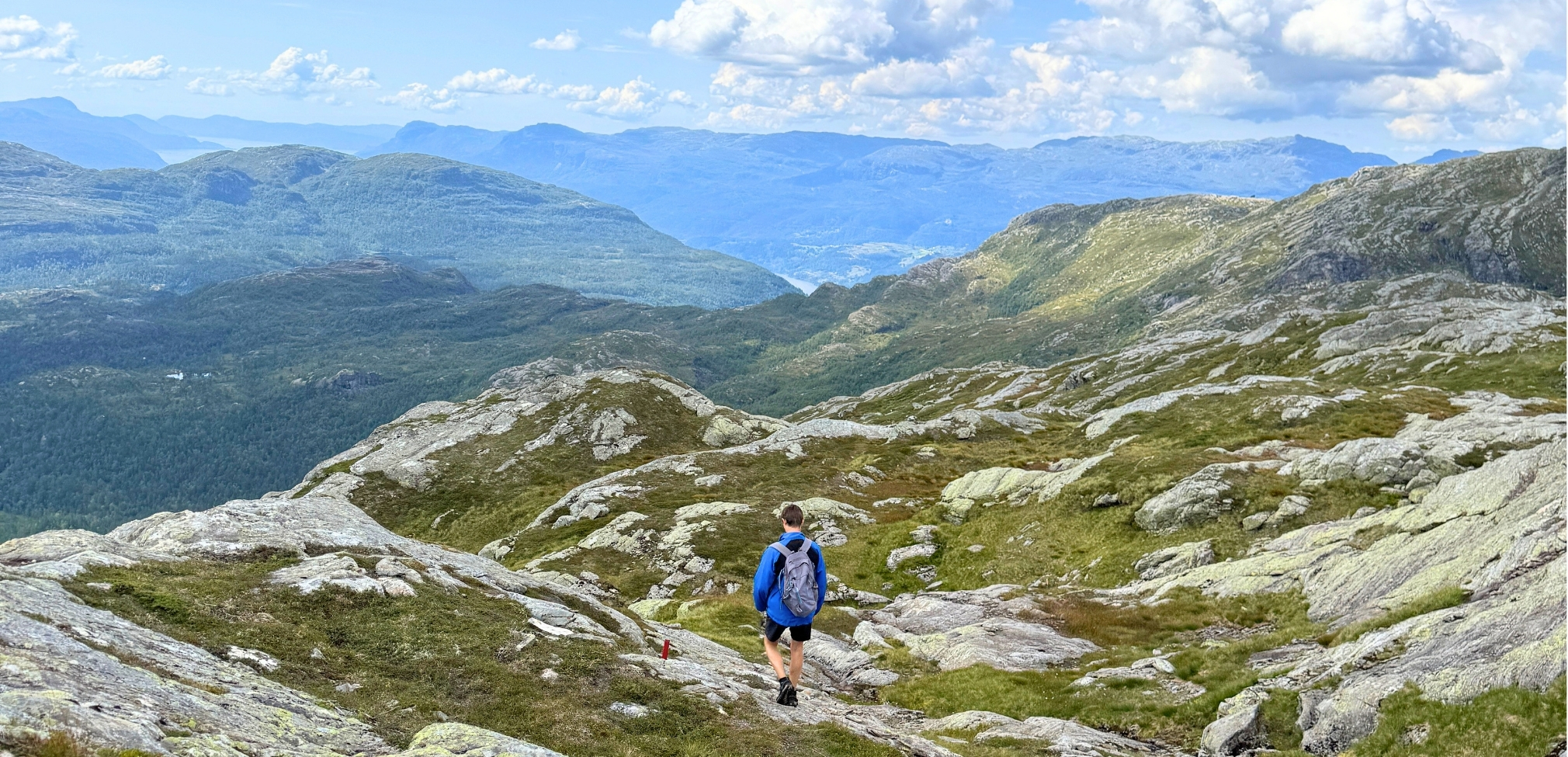 Ein person sit på ein åskam og ser ut over dalen i solnedgangen