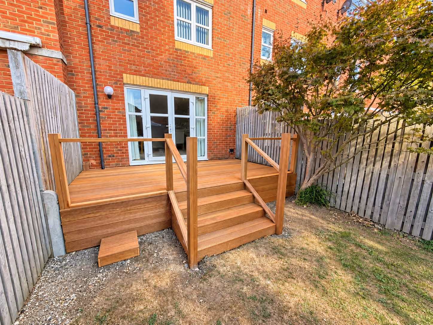 Wide garden view of completed hardwood decking with steps and wooden handrails outside a brick house