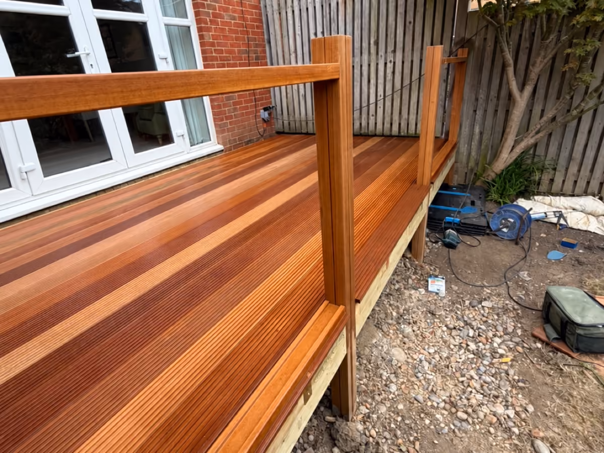View along newly installed timber decking and a wooden handrail beside patio doors during construction