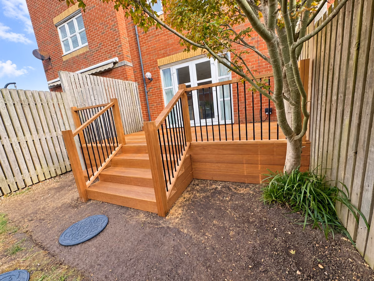 Side view of completed hardwood decking and steps with black metal spindles beside a garden tree