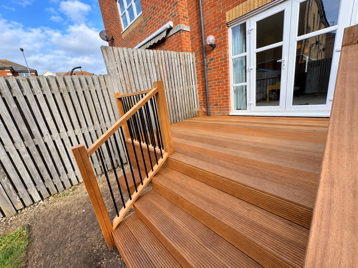Hardwood garden steps leading onto raised decking beside patio doors, with timber handrails and black metal spindles.