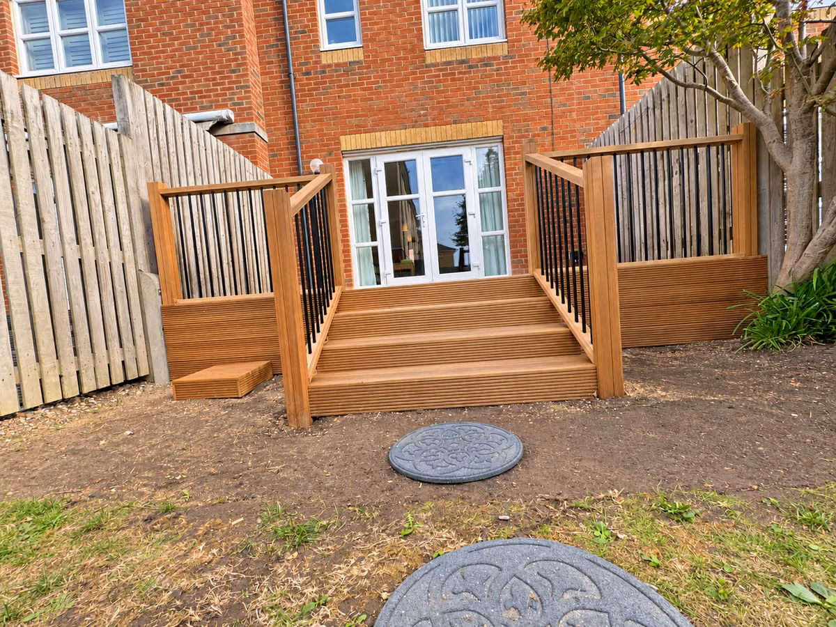Low front view of wide hardwood decking steps with timber handrails and black metal balusters outside patio doors.