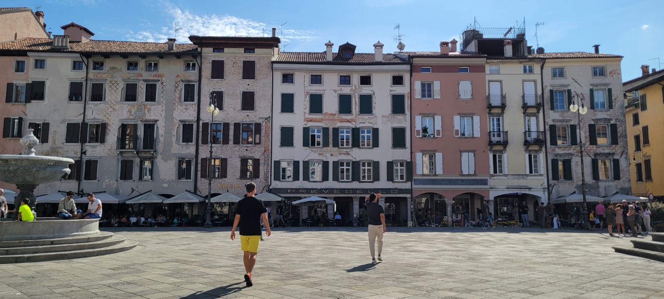 Two men walking in a piazza in Udine looking around at the old buildings.