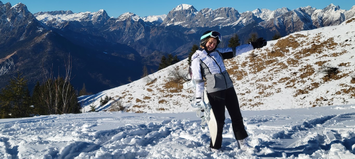 A woman posing in snow holding her snowboard in front of snowy mountains
