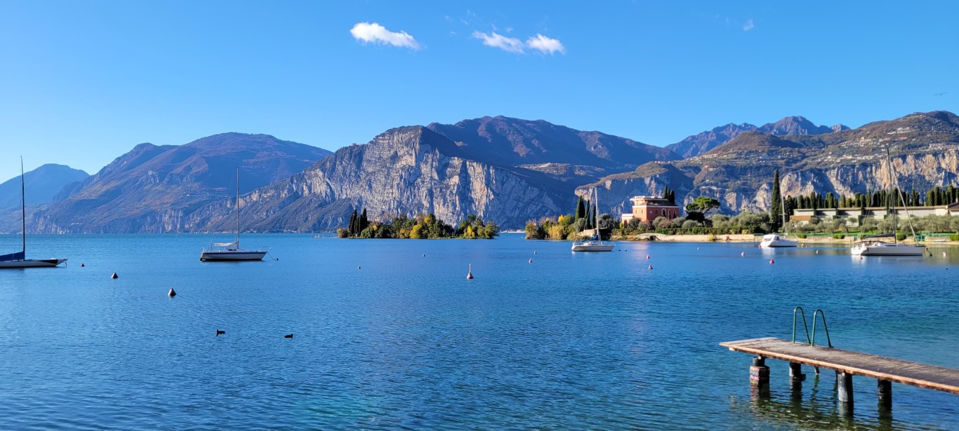A coastal view of Lake Garda with sailboat anchored and a backdrop of steep cliffs coming out from the water.