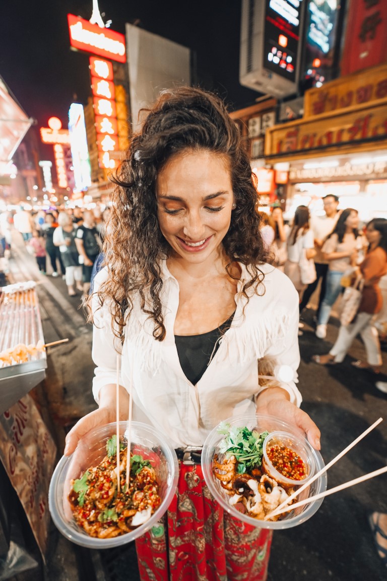 An American expat living in Thailand holding two plates of Thai street food