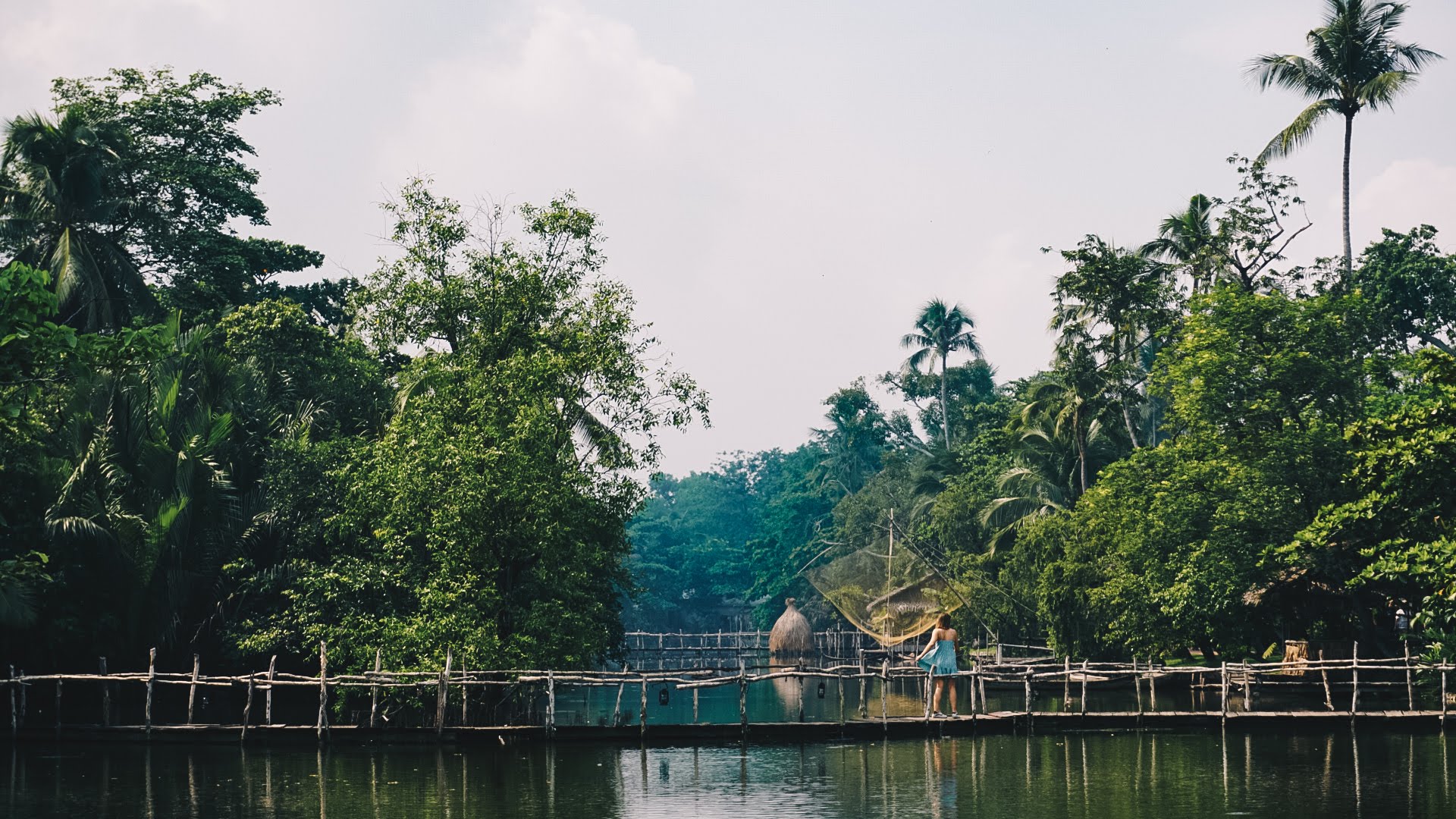 A woman crossing a wooden bridge in an area covered with rivers and lush greenery