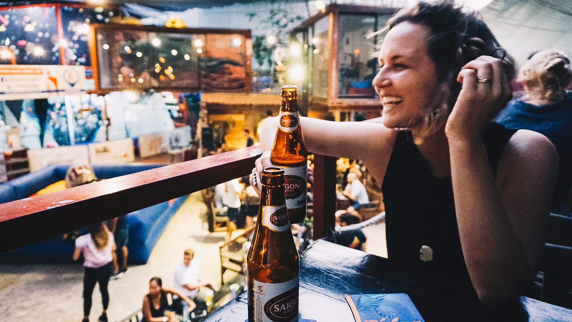 A slightly blurry picture of a woman laughing while drinking a Saigon beer
