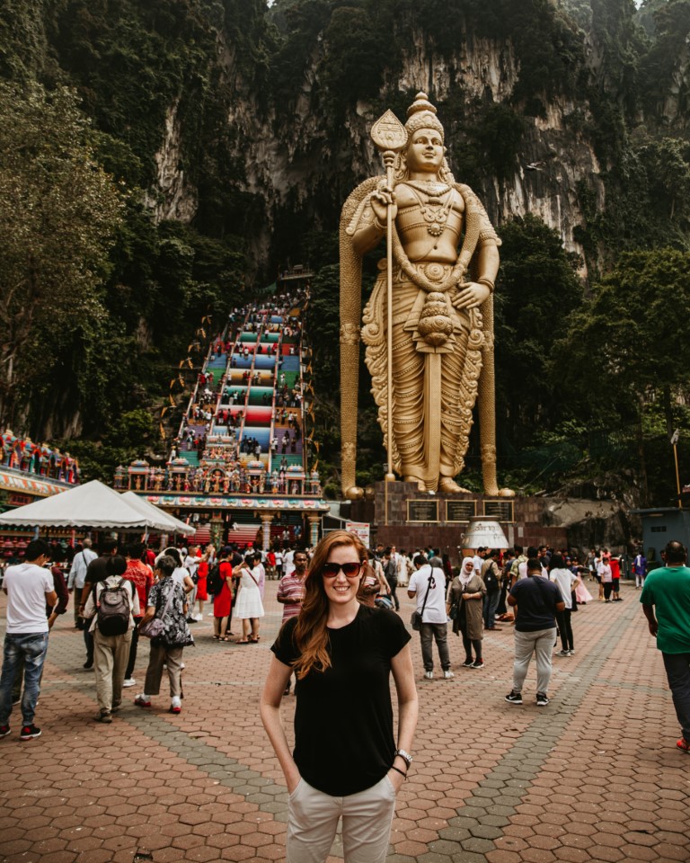 A woman from South Africa posing in front of the rainbow stairs and golden statue at Batu Caves, Malaysia