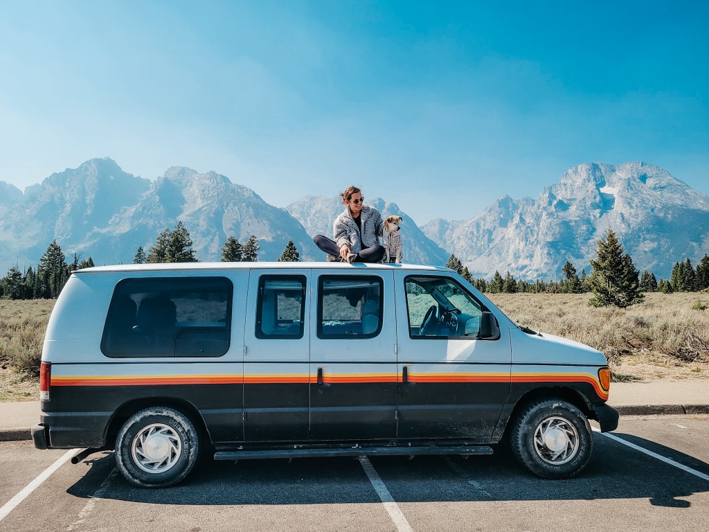 a woman and her dog sitting on top of their converted ford econoline van in the grand tetons