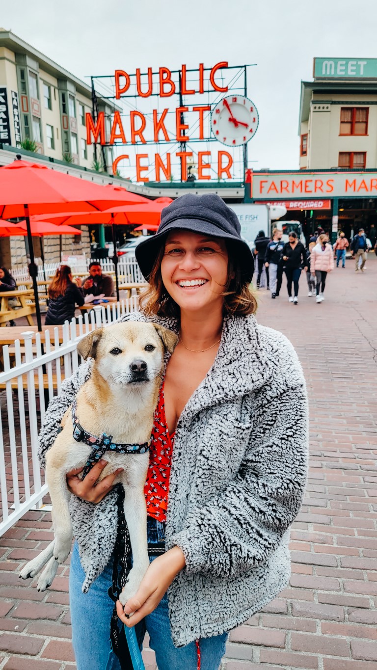 a woman holding her dog in front of pike place market in seattle, washington