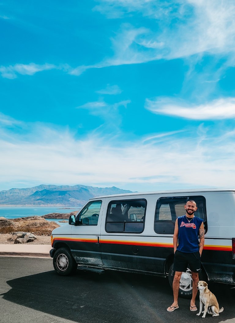 a man posing infront of his converted van with his dog at a lake outside of las vegas, nevada