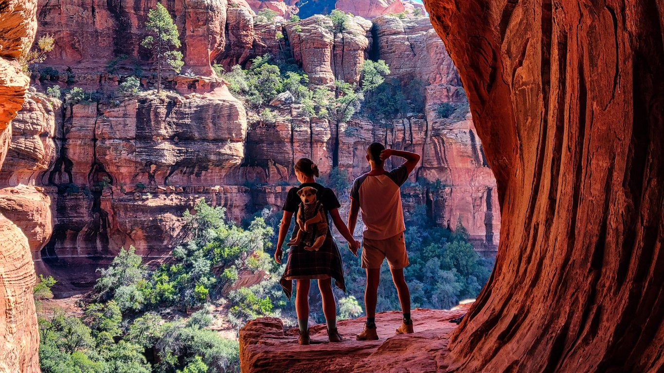 a couple holding hands inside of Subway Cave, with their dog in a backpack on the woman's back