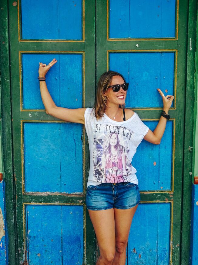 Solo female traveler posing in front of blue and green wooden doors in Cartagena, Colombia