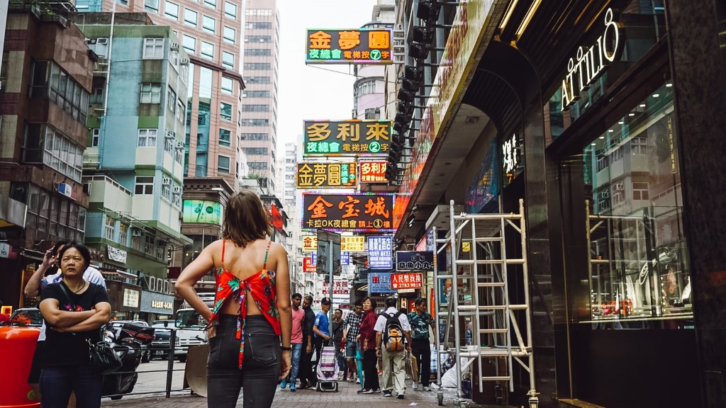 A female tourist standing on the sidewalk in Hong Kong looking at the busy street and neon signs
