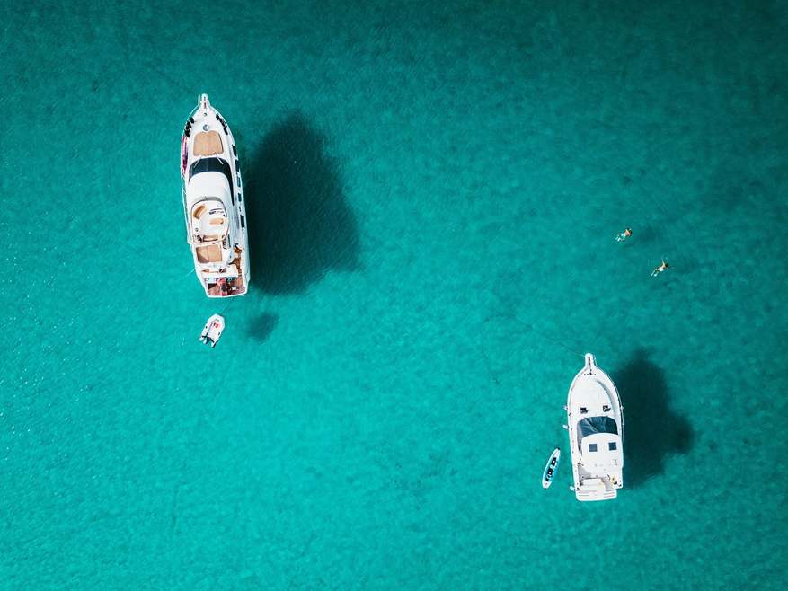 Drone shot of two yachts and two people snorkeling in beautiful, clear water