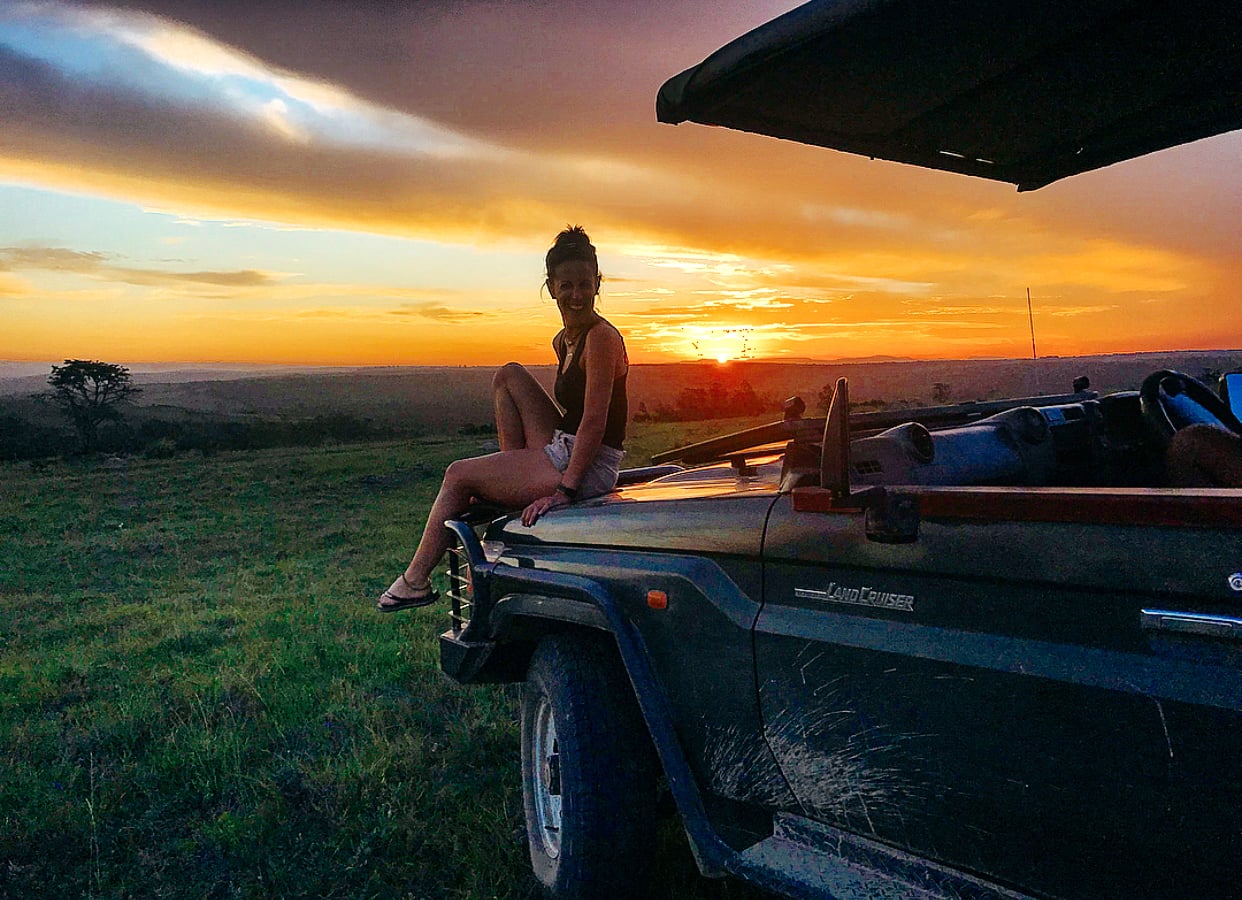 Woman sitting on the front of a jeep, watching the sunset in South Africa