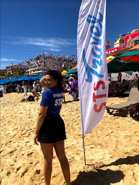 A spring break destination rep at work in Mexico standing in the sand in her uniform